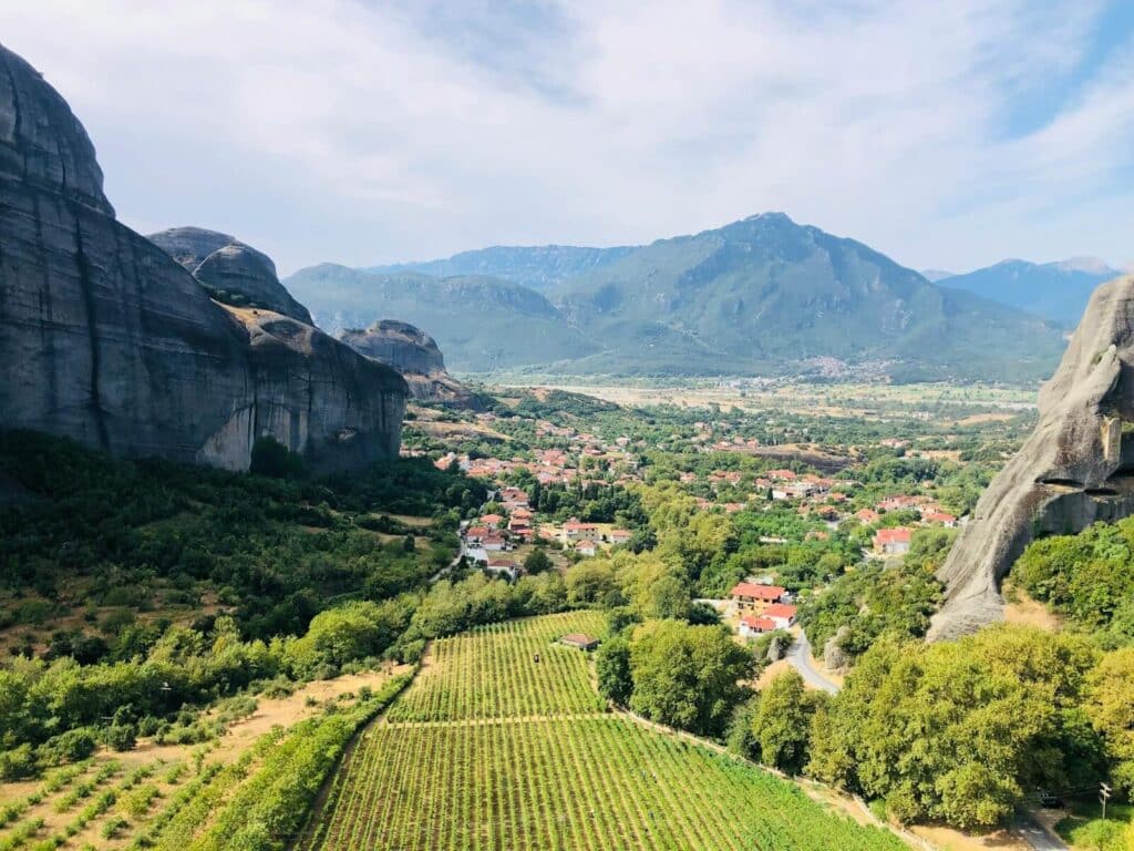 Scenic view of Trikala, Greece featuring lush valley, vineyards, and mountain range.