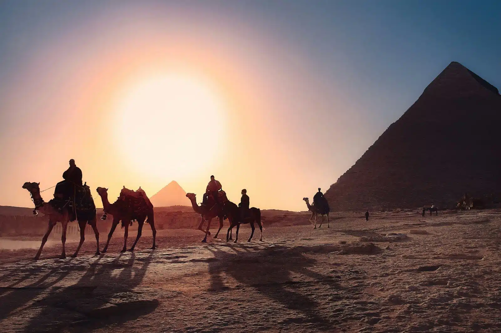 five persons riding camels walking on sand beside Pyramid of Egypt, valley of the kings tour