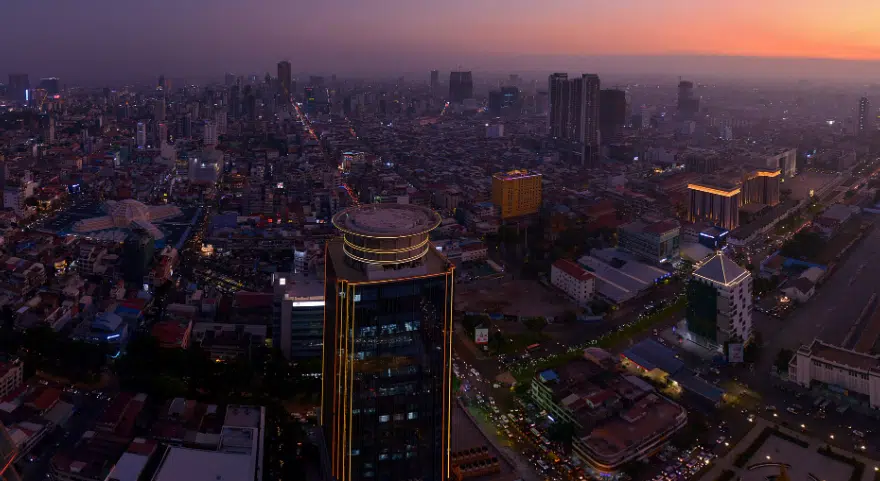 Phnom Penh's skyline lights up at dusk as the sky turns orange over the city.