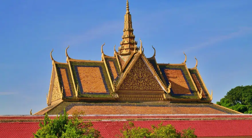 The gilded, tiered roof of Phnom Penh's Royal Palace rises against a clear blue sky.