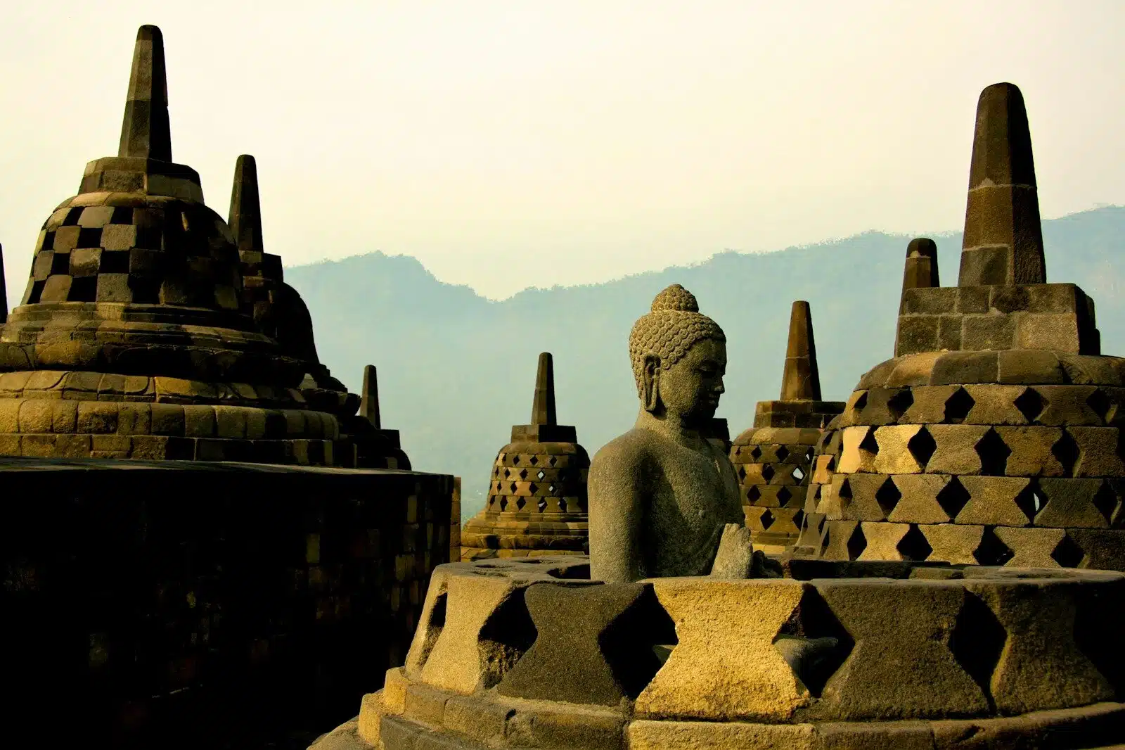 A stone Buddha statue among bell-shaped stupas at Borobudur temple in Indonesia
